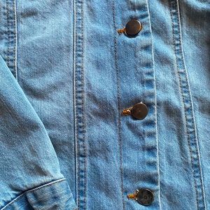 Light blue denim jacket with pockets and “ripped” bottom.